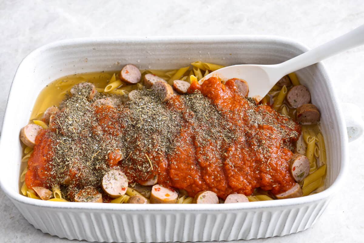 This one-pan Italian Sausage Casserole is the ultimate comfort food! With tender pasta, flavorful sausage, rich marinara, and gooey melted cheese, it’s an easy dinner that’s perfect for busy nights. It's a recipe the whole family will love! Angle shot of chicken broth, and noodles with sausage sauce and seasonings over the top.