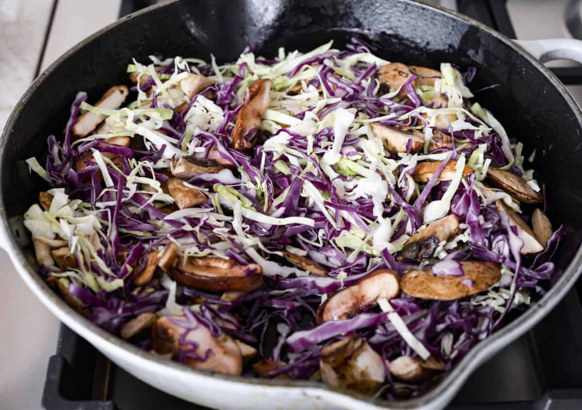 Moo Shu Chicken is a takeout favorite that’s so easy to make at home! This flavorful dish combines tender strips of chicken, mushrooms, and cabbage with a sweet and savory sauce. It’s quick, packed with vibrant flavors, and the perfect weeknight meal! Angle shot of cabbage and mushrooms in a skillet.