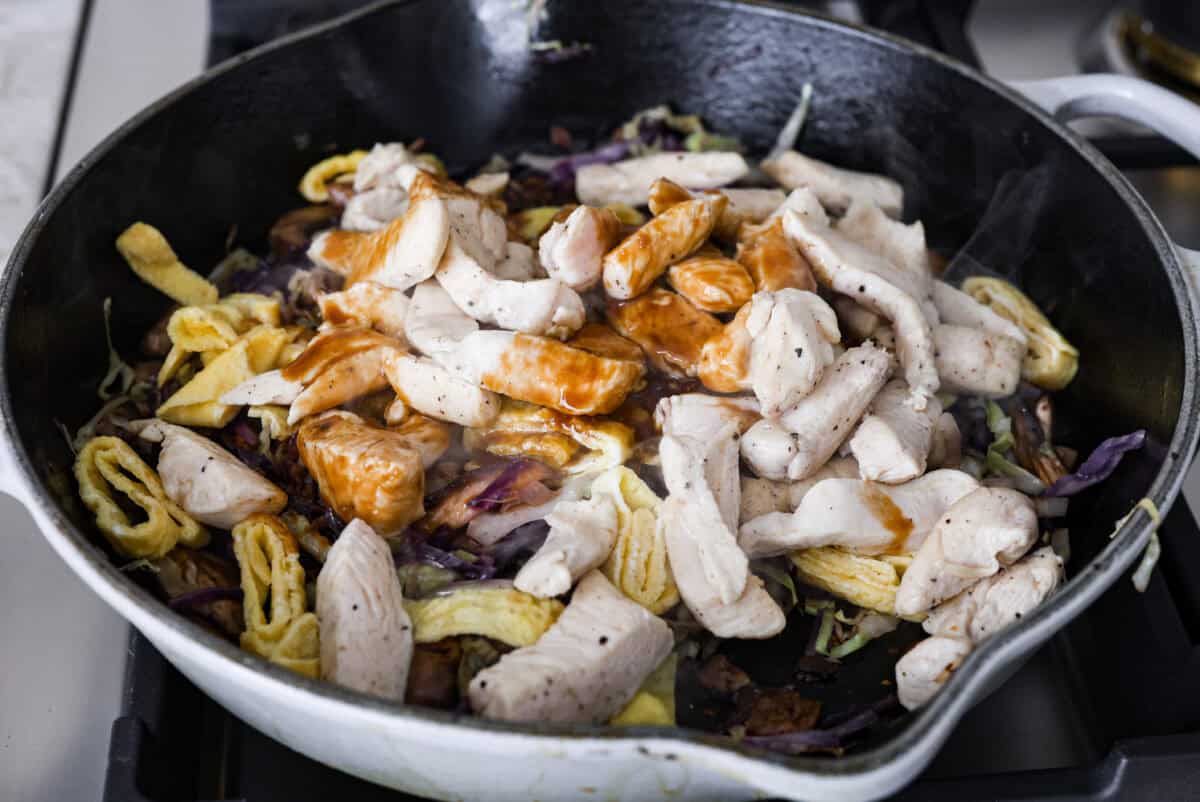 Moo Shu Chicken is a takeout favorite that’s so easy to make at home! This flavorful dish combines tender strips of chicken, mushrooms, and cabbage with a sweet and savory sauce. It’s quick, packed with vibrant flavors, and the perfect weeknight meal! Angle shot of the Moo Shu chicken and eggs added to the cabbage and mushrooms with sauce poured over the top.