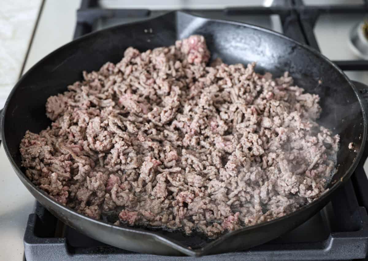Salisbury Steak casserole is a warm and comforting savory dish. It has a thick beef gravy, tender mushrooms, and seasoned hamburger topped with rich, creamy potatoes. Angle shot of ground beef browning in a skillet.