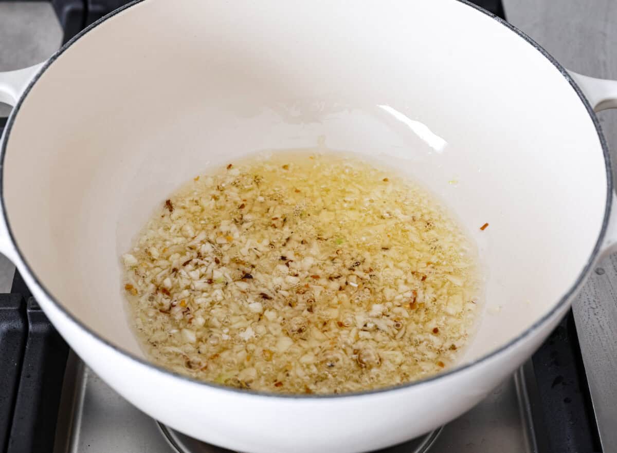 Spaghetti Aglio e Olio uses simple ingredients to create a dish bursting with flavor! With just garlic, olive oil, chili flakes, pasta, and parmesan cheese, this classic Italian recipe is a go-to for a tasty meal in less than 30 minutes. Angle shot of olive oil, garlic and red pepper flakes sautรฉing in a pot on the stove.