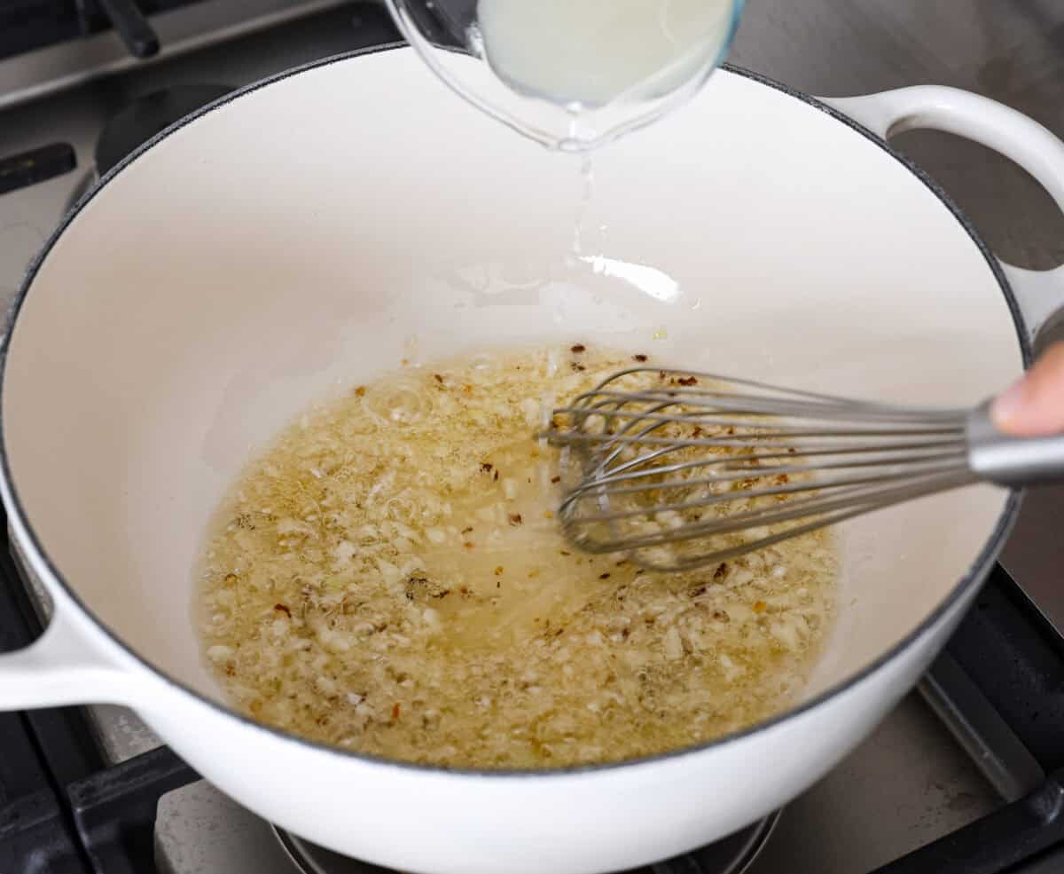 Spaghetti Aglio e Olio uses simple ingredients to create a dish bursting with flavor! With just garlic, olive oil, chili flakes, pasta, and parmesan cheese, this classic Italian recipe is a go-to for a tasty meal in less than 30 minutes. Angle shot of someone whisking the pasta water in with the olive oil, garlic and red pepper flakes.