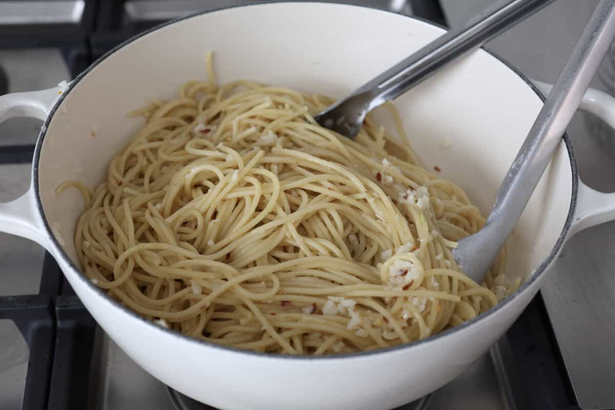 Spaghetti Aglio e Olio uses simple ingredients to create a dish bursting with flavor! With just garlic, olive oil, chili flakes, pasta, and parmesan cheese, this classic Italian recipe is a go-to for a tasty meal in less than 30 minutes. Angle shot of someone stirring noodles in the pot with the sauce.