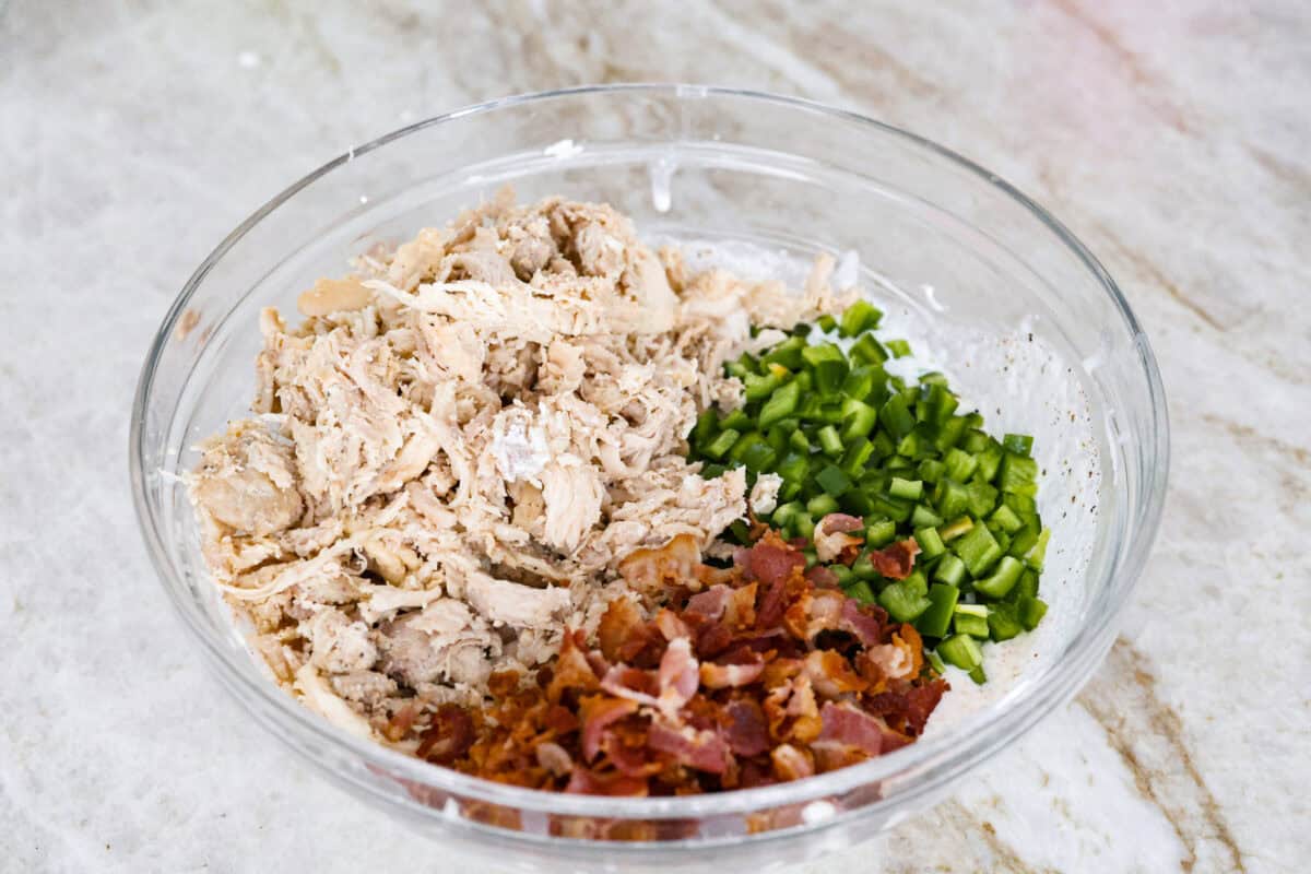 Spice up dinnertime with this creamy Jalapeño Popper Casserole! Packed with tender chicken, melty cheese, and just the right kick of heat, it's hearty and so easy to make. Delicious comfort food with a spicy twist! Angle shot of cooked chicken, jalapeños, and bacon in a bowl.