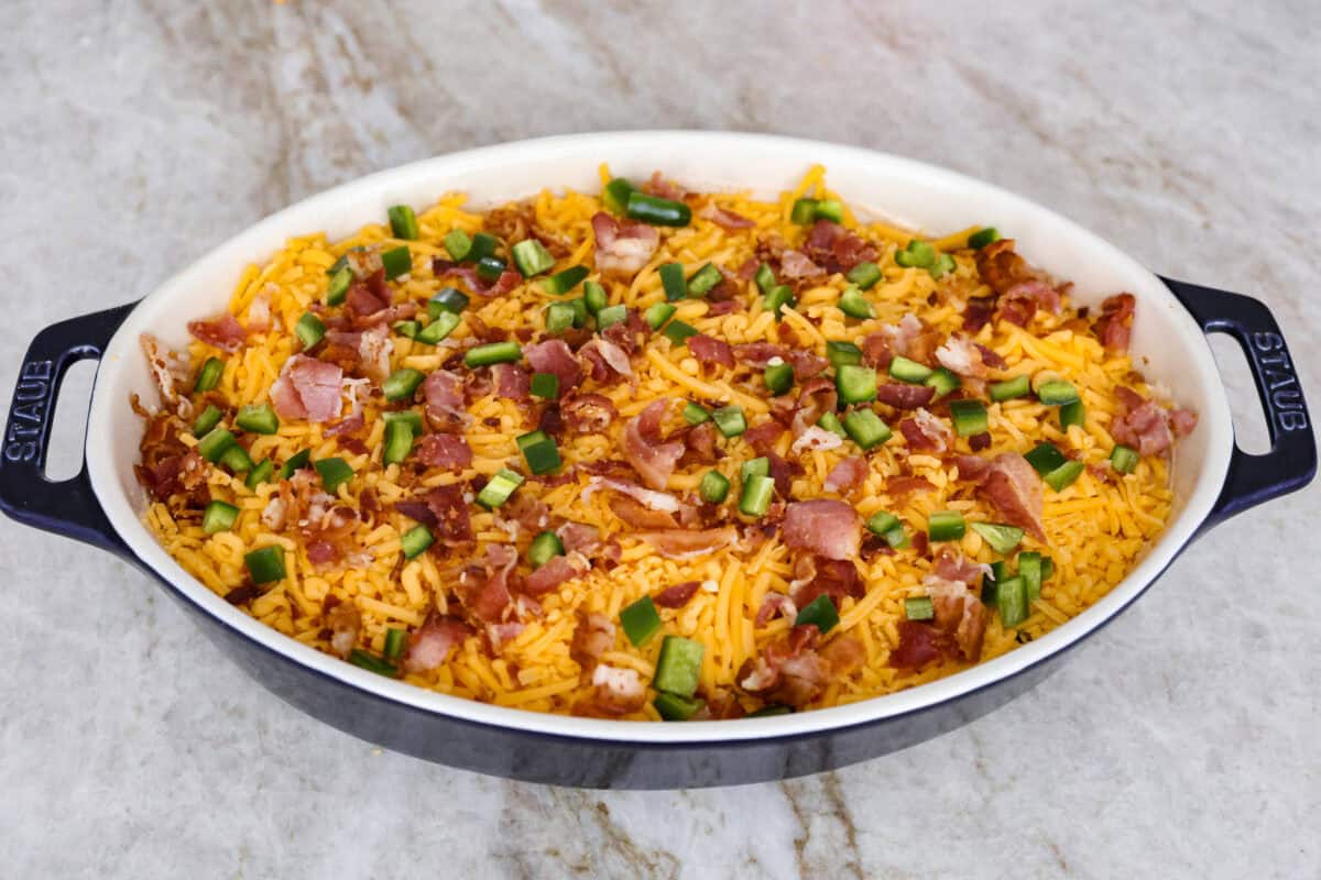 Spice up dinnertime with this creamy Jalapeño Popper Casserole! Packed with tender chicken, melty cheese, and just the right kick of heat, it's hearty and so easy to make. Delicious comfort food with a spicy twist! Angle shot of the cheese bacon and jalapeños sprinkled over the top of the chicken and cream cheese mixture.