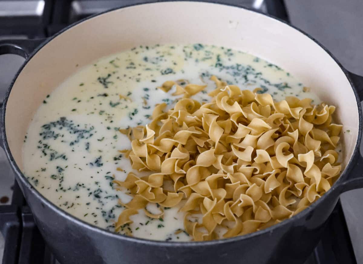 This creamy chicken noodle soup tastes exactly how it sounds! It's classic chicken noodle soup but creamy, rich and filling! Loaded with hearty chicken, tender carrots, supple noodles, and lots of delicious flavors, it's perfect for winter! Angle shot of cream chicken broth vegetables and seasoning in a pot with egg noodles added on top.