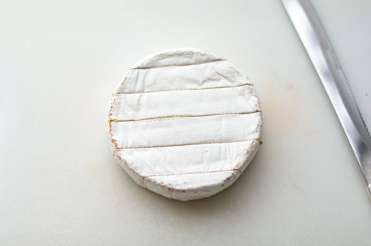 Warm and gooey baked brie is a hit for any occasion! With just five simple ingredients and less than 20 minutes, you will have a rich, creamy appetizer that's impossible to resist. Scoop it up with your favorite crackers or bread! Overhead shot of a circle of brie cheese with horizontal slices through the top.