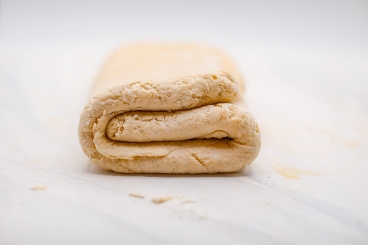 Biscuit Cinnamon Rolls are the most amazing twist on a classic! They are perfectly light, fluffy, and packed with cinnamon. The texture is more flakey and moist than traditional cinnamon rolls! Whether it’s for a cozy weekend breakfast or a holiday brunch, these hit the spot! Side shot of biscuit cinnamon roll dough folded into a tri-fold.