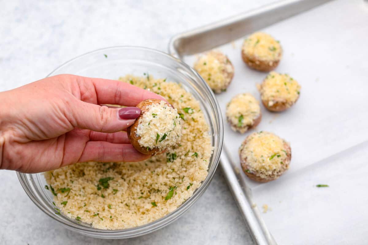 Boursin stuffed mushrooms are a fun, delicious appetizer or side dish. These creamy, cheesy stuffed mushrooms are packed with flavorful Boursin cheese and topped with a delightful breadcrumb crunch. Overhead shot of someone holding a putting bread crumbs onto the cheese stuffed mushroom.