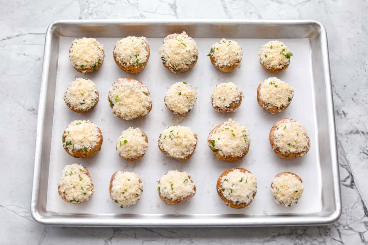 Boursin stuffed mushrooms are a fun, delicious appetizer or side dish. These creamy, cheesy stuffed mushrooms are packed with flavorful Boursin cheese and topped with a delightful breadcrumb crunch. Overhead shot of evenly spaced mushrooms on a cookie sheet.