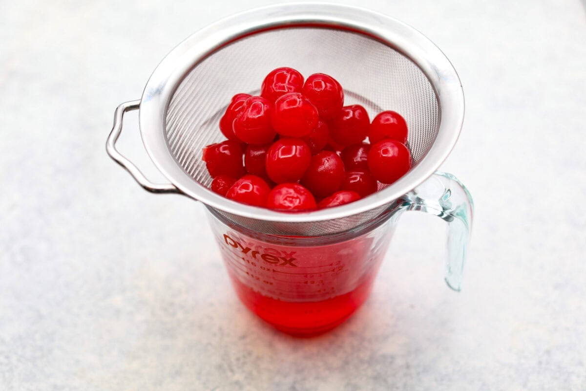 Homemade cherry cordials are a tasty, nostalgic treat! They're made with sweet cherries that are coated in a rich chocolate shell. Make them for Christmas or Valentineโs Day, and watch them disappear! Angle shot of cherries in a strainer over a measureing cup.