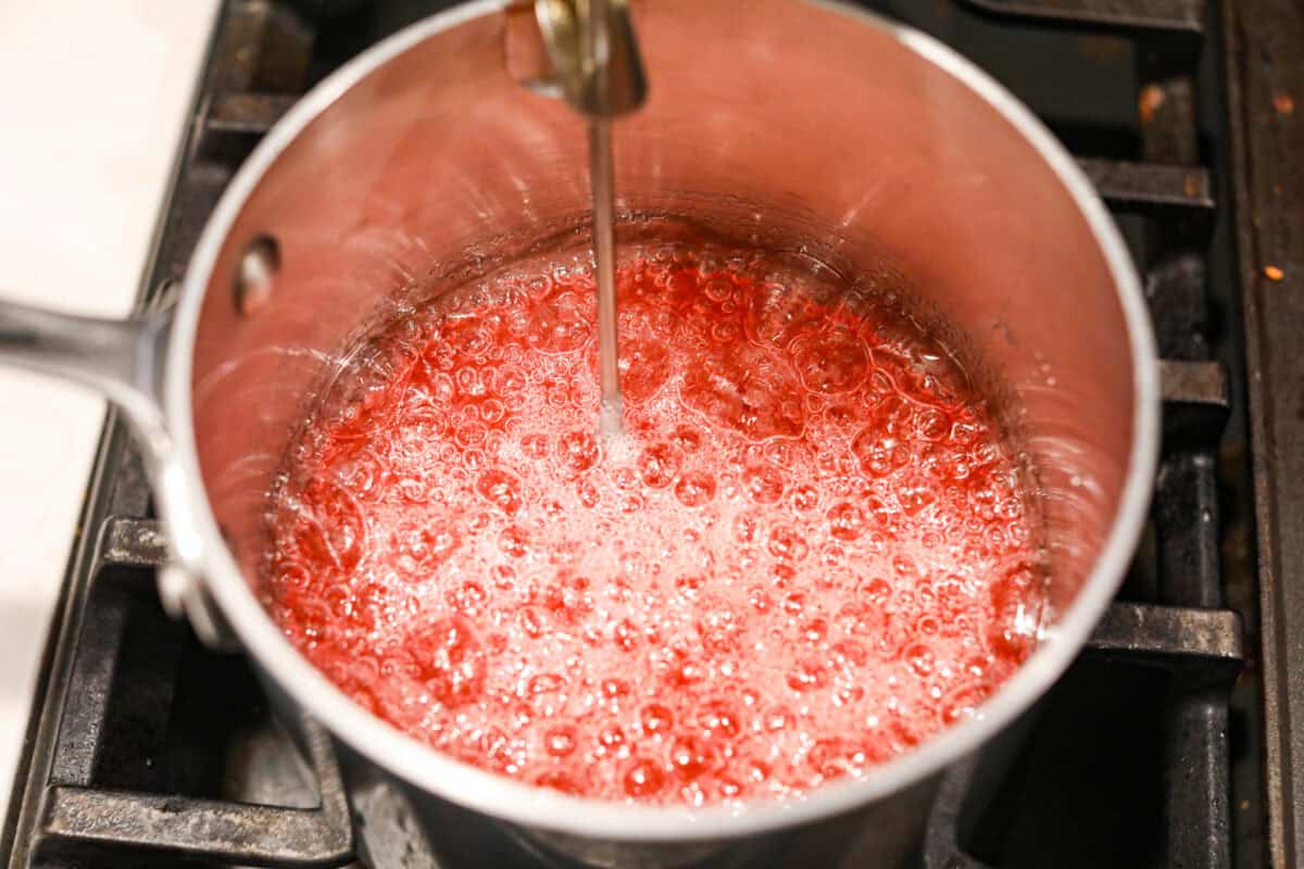 Homemade cherry cordials are a tasty, nostalgic treat! They're made with sweet cherries that are coated in a rich chocolate shell. Make them for Christmas or Valentineโs Day, and watch them disappear! Angle shot of sugars boiling in the saucepan with a candy thermometer sticking out.