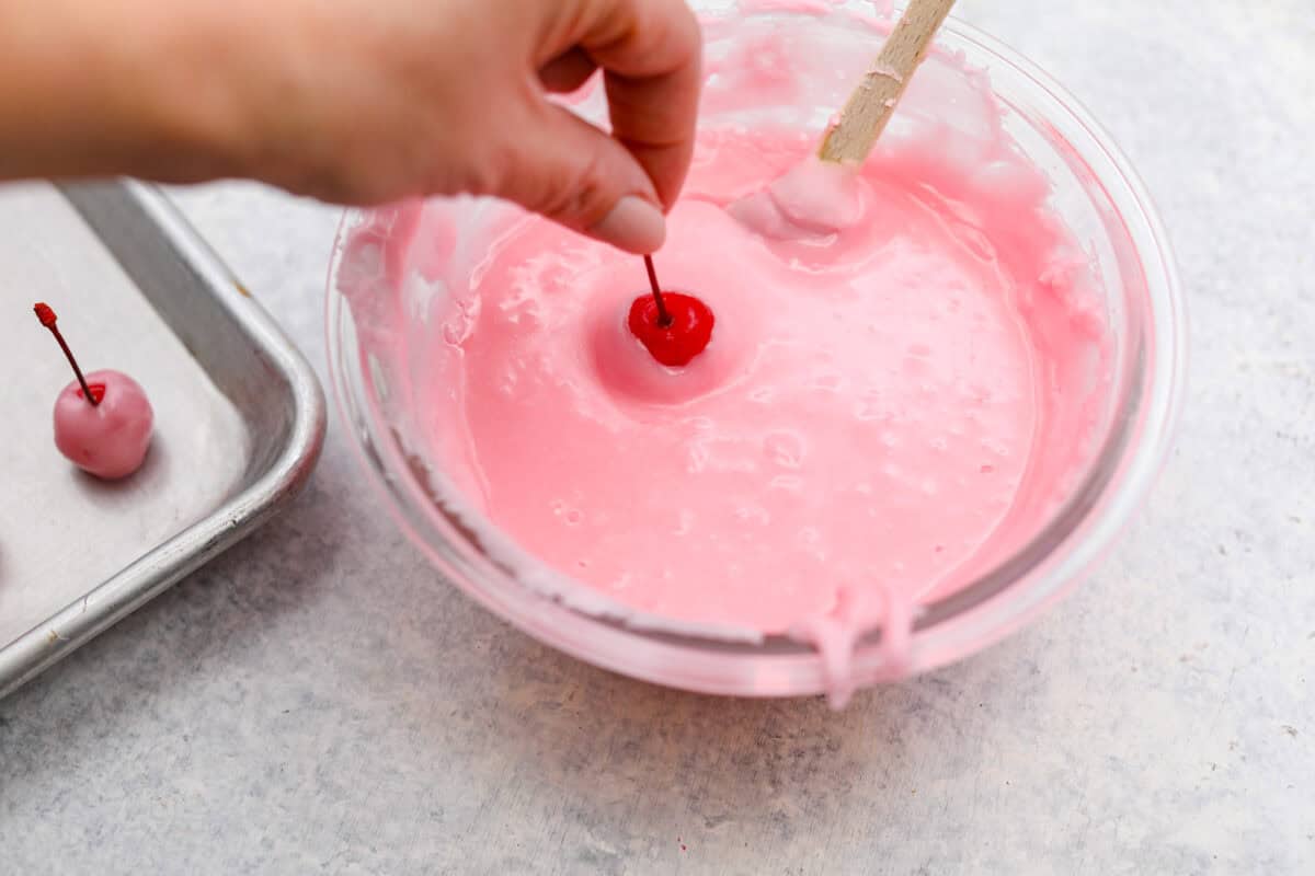 Homemade cherry cordials are a tasty, nostalgic treat! They're made with sweet cherries that are coated in a rich chocolate shell. Make them for Christmas or Valentineโs Day, and watch them disappear! Angel shot of someone dipping cherries into the fondant.