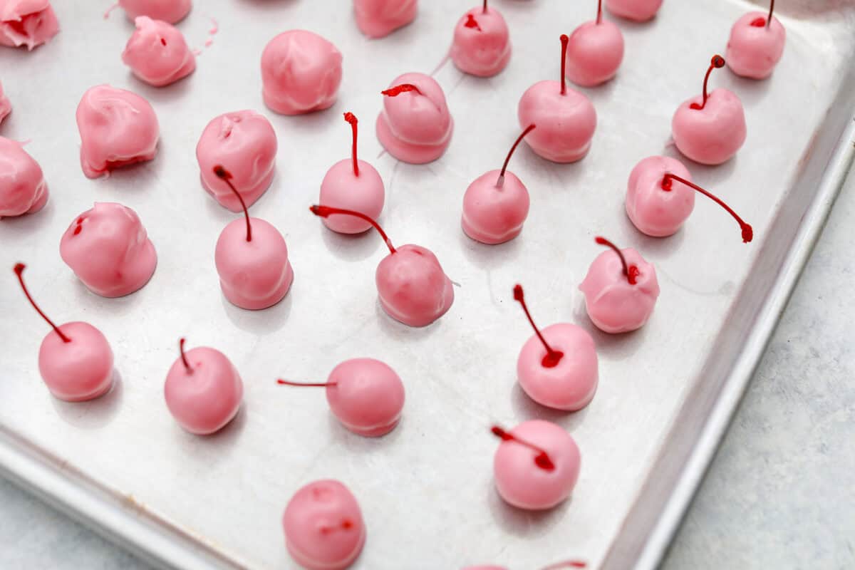 Homemade cherry cordials are a tasty, nostalgic treat! They're made with sweet cherries that are coated in a rich chocolate shell. Make them for Christmas or Valentineโs Day, and watch them disappear! Overhead shot of fondant dipped cherries on a baking sheet.