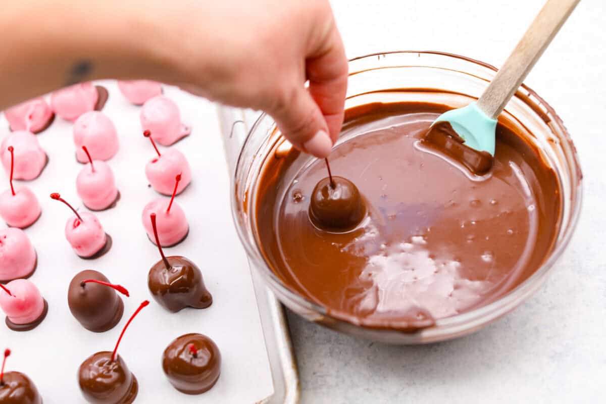 Homemade cherry cordials are a tasty, nostalgic treat! They're made with sweet cherries that are coated in a rich chocolate shell. Make them for Christmas or Valentineโs Day, and watch them disappear! Angle shot of someone holding a chocolate dipped cherry over the bowl of chocolate.
