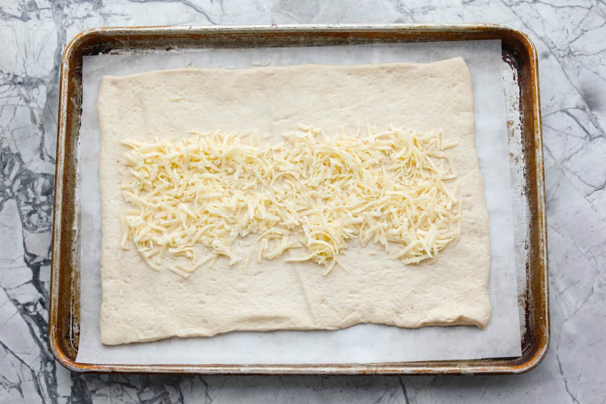 This Chicken Bacon Ranch Stromboli combines the tasty trio of tender chicken, crispy bacon, and creamy ranch dressing, all wrapped in golden pizza dough. It’s quick to prep and packed with flavor. Overhead shot of the canned pizza dough rolled out with mozzarella cheese down the middle all on parchment-lined cookie sheet.