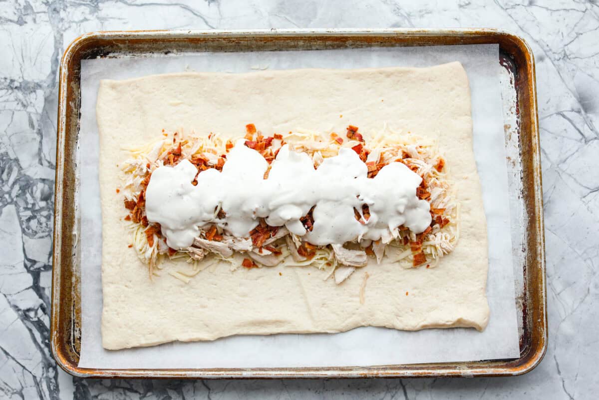 This Chicken Bacon Ranch Stromboli combines the tasty trio of tender chicken, crispy bacon, and creamy ranch dressing, all wrapped in golden pizza dough. It’s quick to prep and packed with flavor. Overhead shot of chicken bacon and ranch spread over the mozzarella.