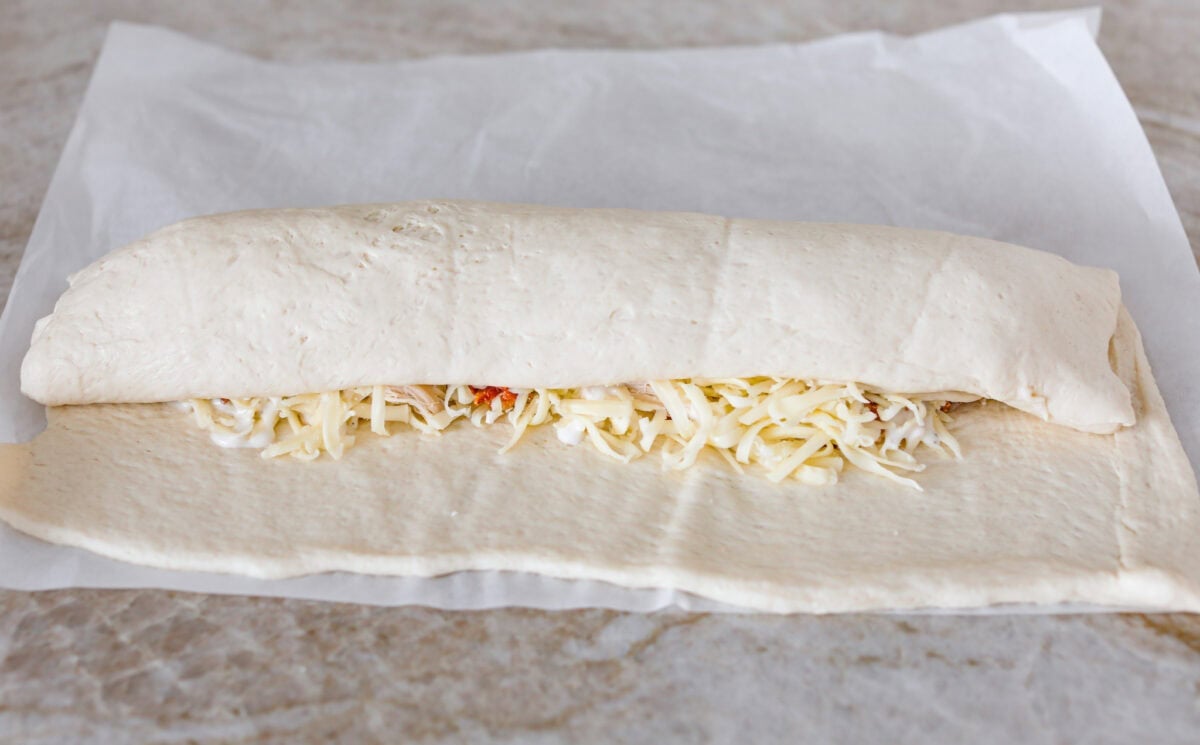 This Chicken Bacon Ranch Stromboli combines the tasty trio of tender chicken, crispy bacon, and creamy ranch dressing, all wrapped in golden pizza dough. It’s quick to prep and packed with flavor. Angel shot of half the pizza dough being folded over the filling.