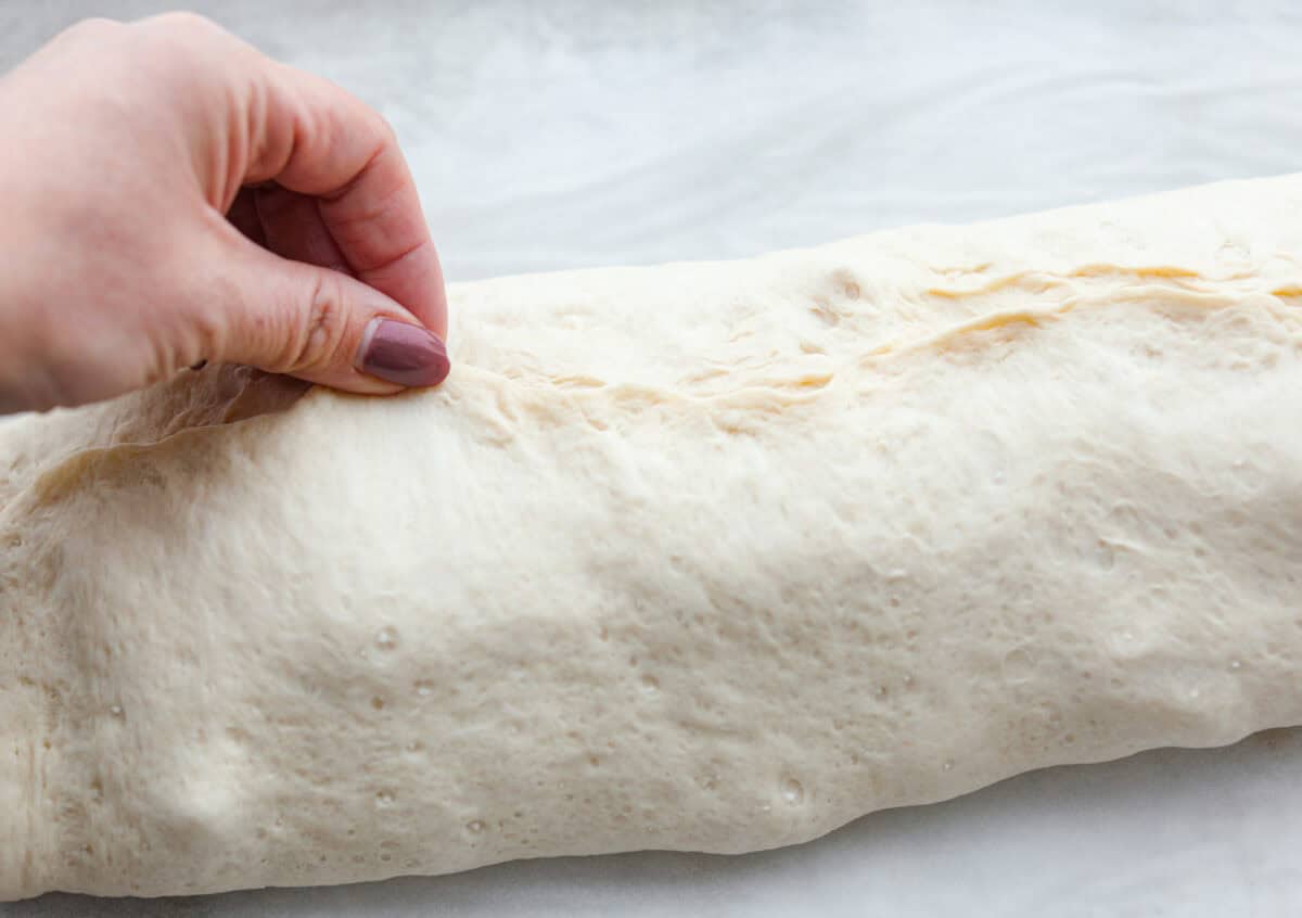 This Chicken Bacon Ranch Stromboli combines the tasty trio of tender chicken, crispy bacon, and creamy ranch dressing, all wrapped in golden pizza dough. It’s quick to prep and packed with flavor. Angel shot of someone pinching together both halves of the pizza dough surrounding the filling.