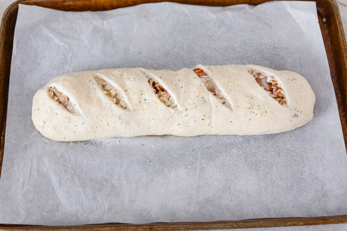 This Chicken Bacon Ranch Stromboli combines the tasty trio of tender chicken, crispy bacon, and creamy ranch dressing, all wrapped in golden pizza dough. It’s quick to prep and packed with flavor. Angle shot of the Stromboli covered and cut and ready to go in the oven.