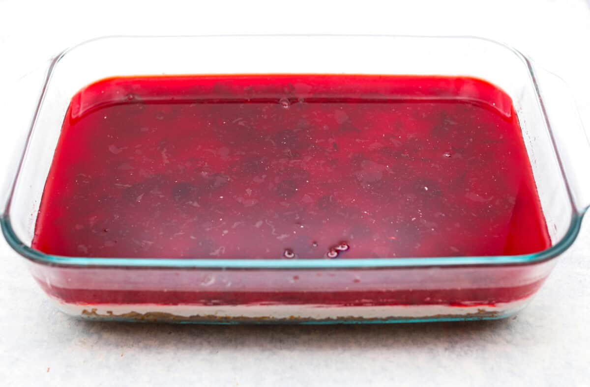 Make this festive cranberry pretzel salad for the holidays! The salty pretzel crust is the perfect balance to the sweet and creamy layers. Cranberry sauce gives it a pop of tartness and makes it holiday-ready! Seventh photo of the jello poured over the cream cheese layer.