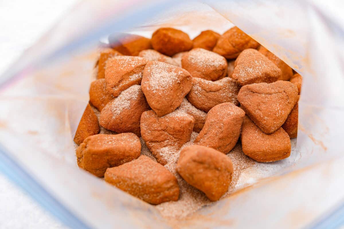 Crockpot monkey bread is an easy, gooey treat made in your slow cooker. It’s packed with soft biscuit pieces, cinnamon-sugar flavor, and a sweet buttery glaze. No oven needed! Overhead shot of biscuit dough in a ziploc bag with cinnamon and sugar.