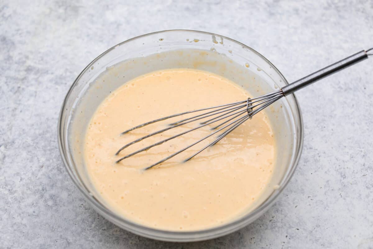 Eggnog Poke Cake could not be more perfect for the holiday season! It combines the rich flavor of eggnog with the soft, moist texture of a classic poke cake. Add fluffy whipped topping and a sprinkle of nutmeg and cinnamon to really wow your family! Overhead shot of topping ingredients whisked together in a bowl.