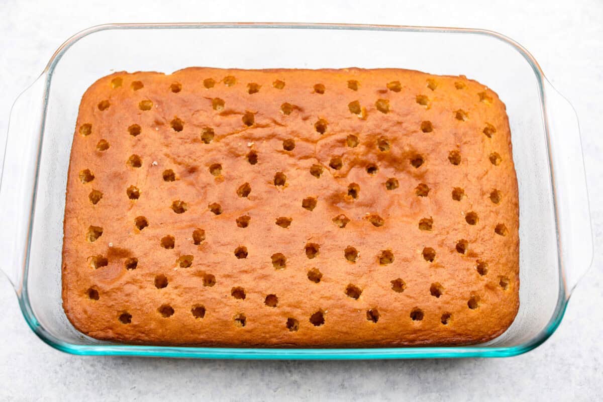 Eggnog Poke Cake could not be more perfect for the holiday season! It combines the rich flavor of eggnog with the soft, moist texture of a classic poke cake. Add fluffy whipped topping and a sprinkle of nutmeg and cinnamon to really wow your family! Overhead shot of the baked cake with holes poked in it.