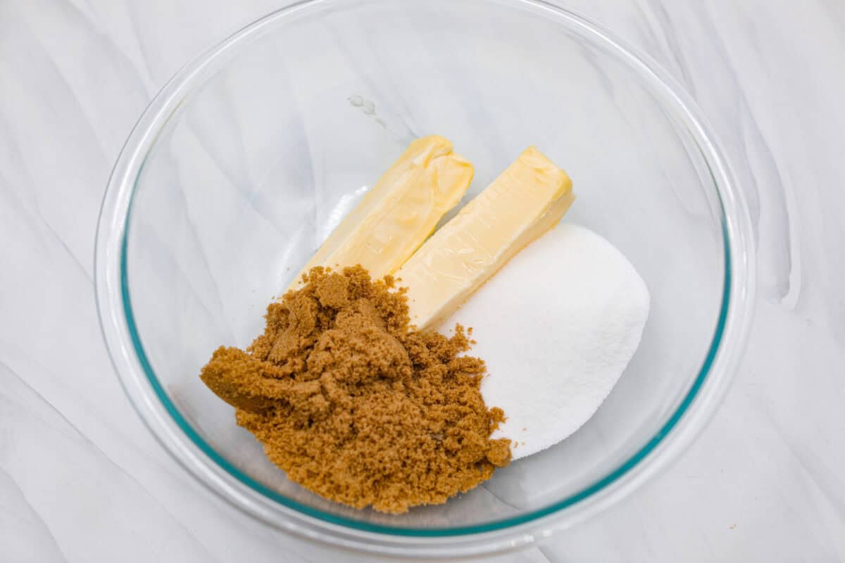 These gingerbread crinkle cookies are incredibly soft and flavorful! Their deep molasses flavor, spiced to perfection and rolled in powdered sugar, is so good with a glass of milk. They are the perfect cookies to make for Santa this holiday season. Overhead shot of butter and sugars in a bowl.
