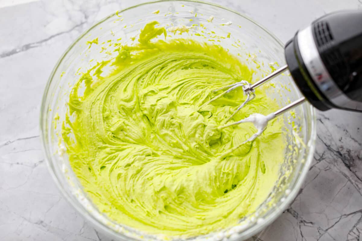 Grinch dip is a sweet and scrumptious dip perfect for any holiday party or gathering. It combines delicious cake mix, fluffy whipped topping, and smooth yogurt or pudding to create a fun dip for cookies, treats, or fruit. Overhead shot of ingredients all mixed together.