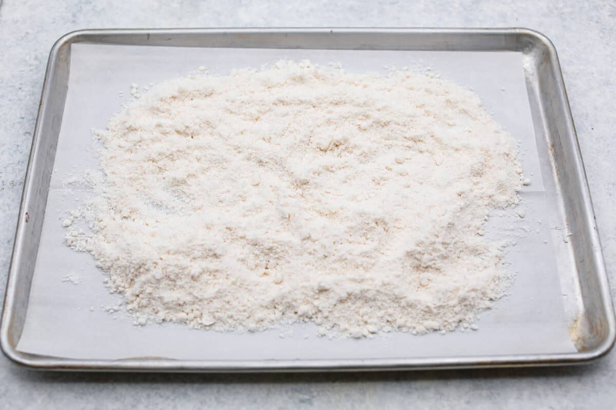 Grinch dip is a sweet and scrumptious dip perfect for any holiday party or gathering. It combines delicious cake mix, fluffy whipped topping, and smooth yogurt or pudding to create a fun dip for cookies, treats, or fruit. Overhead shot of cake mix spread out on a baking sheet to be heat-treated.