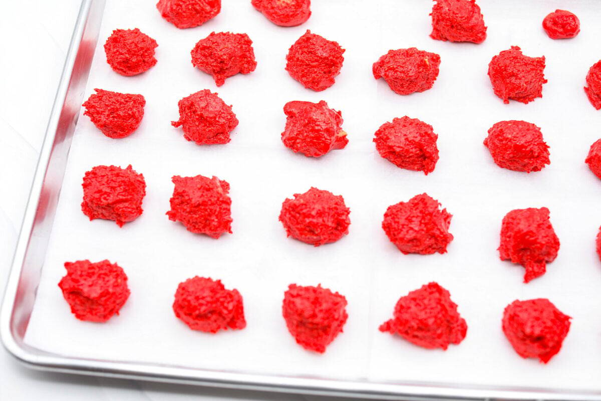These are the cutest Grinch Oreo balls you have ever seen! Fudgy Oreo filling is coated in green candy melts and garnished with the cutest red heart sprinkle. They taste amazing and will steal the show this holiday season at holiday parties, family get-togethers, or Christmas events. Overhead shot of Oreo grinch balls of filling on a parchment lines cookie sheet.