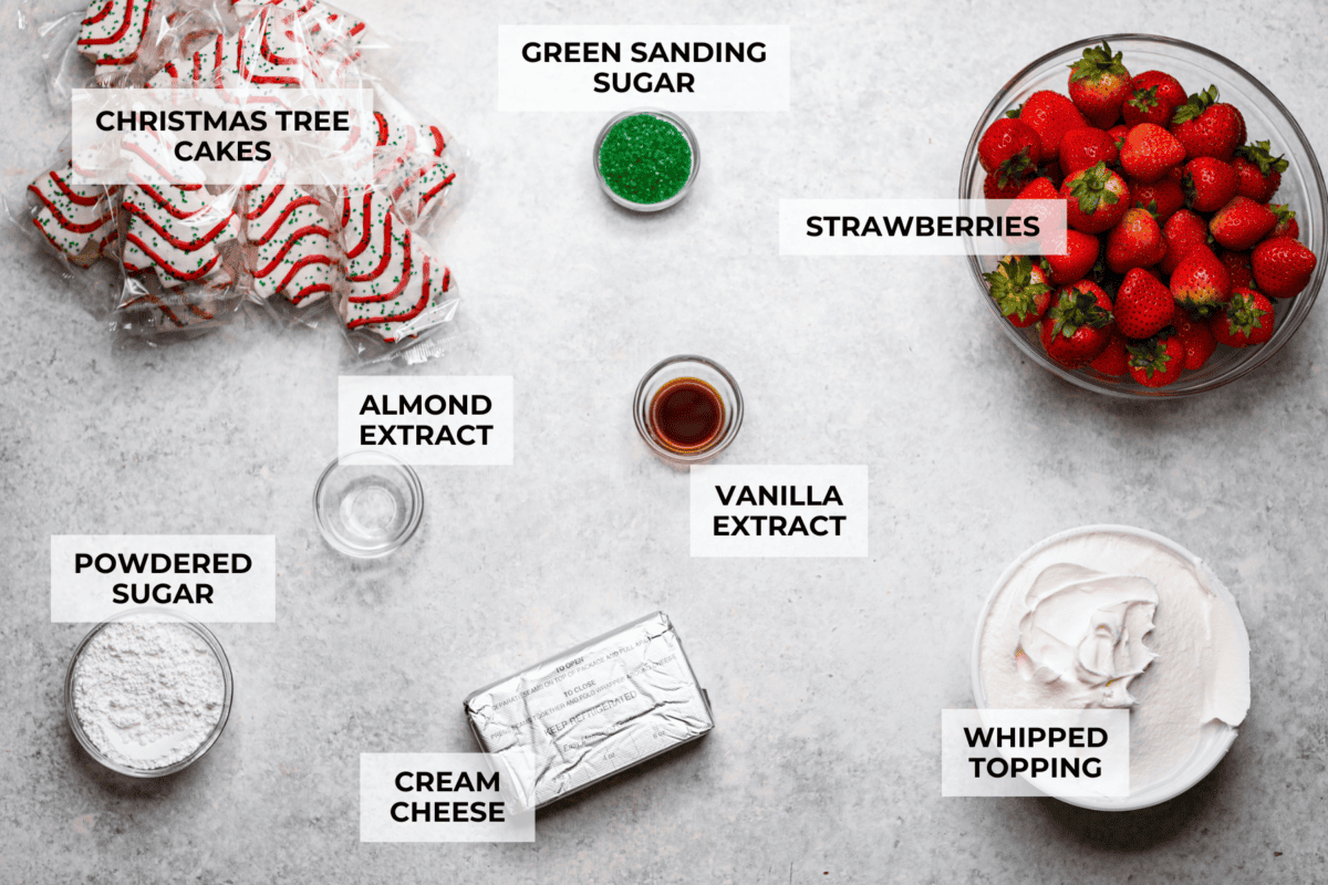 Little Debbie Christmas tree trifle is super adorable and tastes amazing! It's filled with sweet strawberries, creamy cream cheese, whipped topping flavored fluff, and chunks of the iconic Little Debbie Christmas trees. Overhead shot of labeled ingredients.