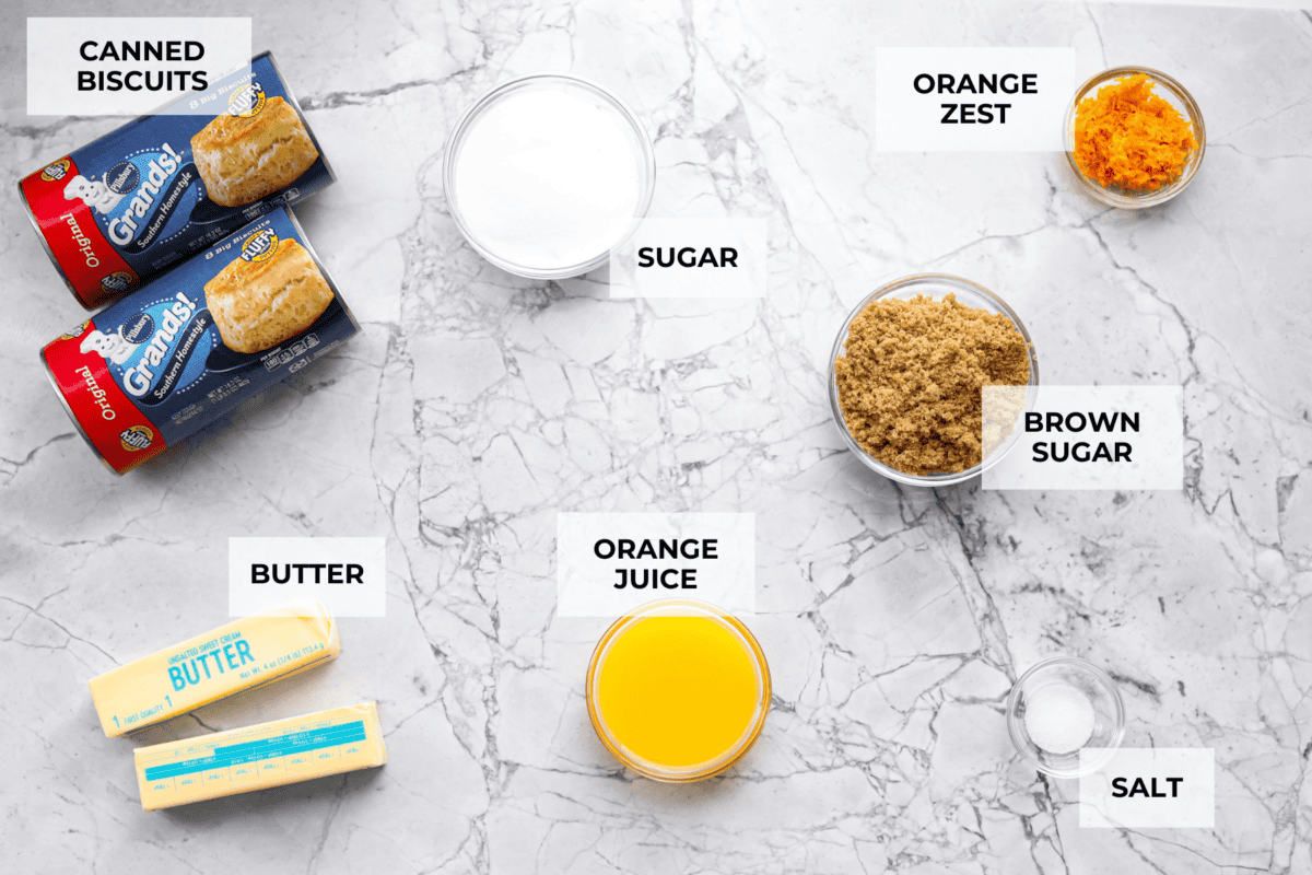 Orange monkey bread is a fun twist on a classic sticky pull-apart bread. It's packed with soft, buttery biscuit pieces, bursts of citrusy orange zest, and a sticky, sweet glaze. Everyone will want to get their hands on this delicious dish! Overhead shot of labeled ingredients.