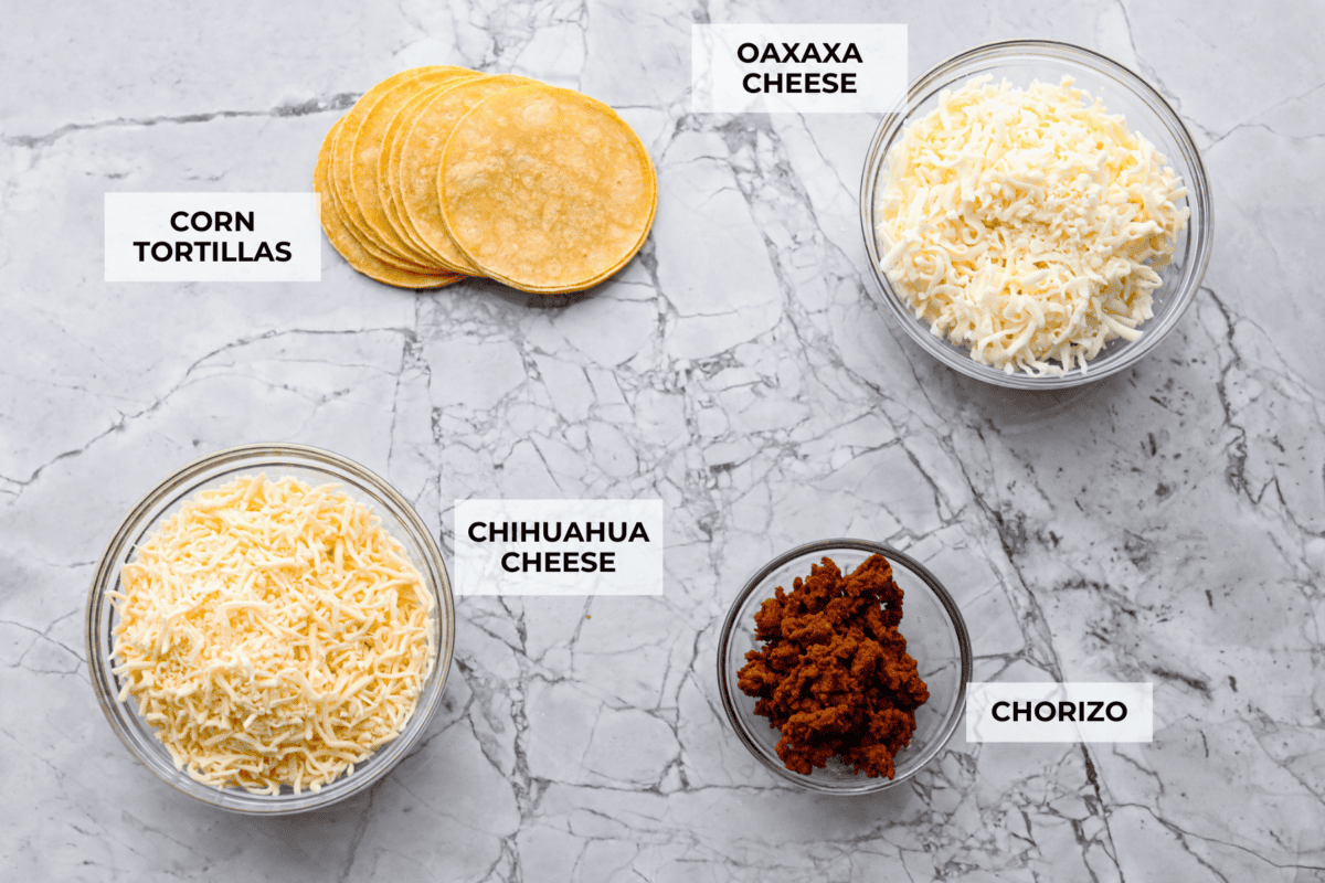 Queso Fundido is a delicious cheesy appetizer with a kick from the Mexican chorizo. It's loaded with buttery, melty cheeses and covered in spicy chorizo sausage. Overhead shot of labeled ingredients.