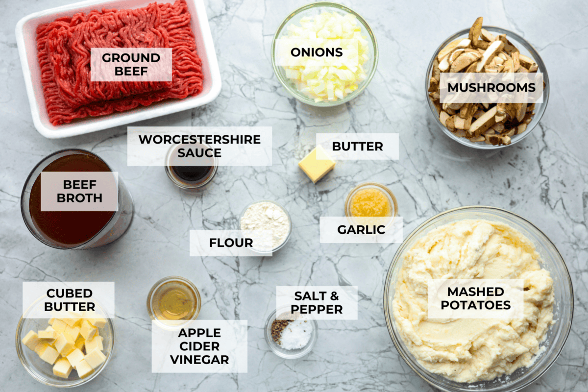 Salisbury Steak casserole is a warm and comforting savory dish. It has a thick beef gravy, tender mushrooms, and seasoned hamburger topped with rich, creamy potatoes. Overhead shot of labeled ingredients.