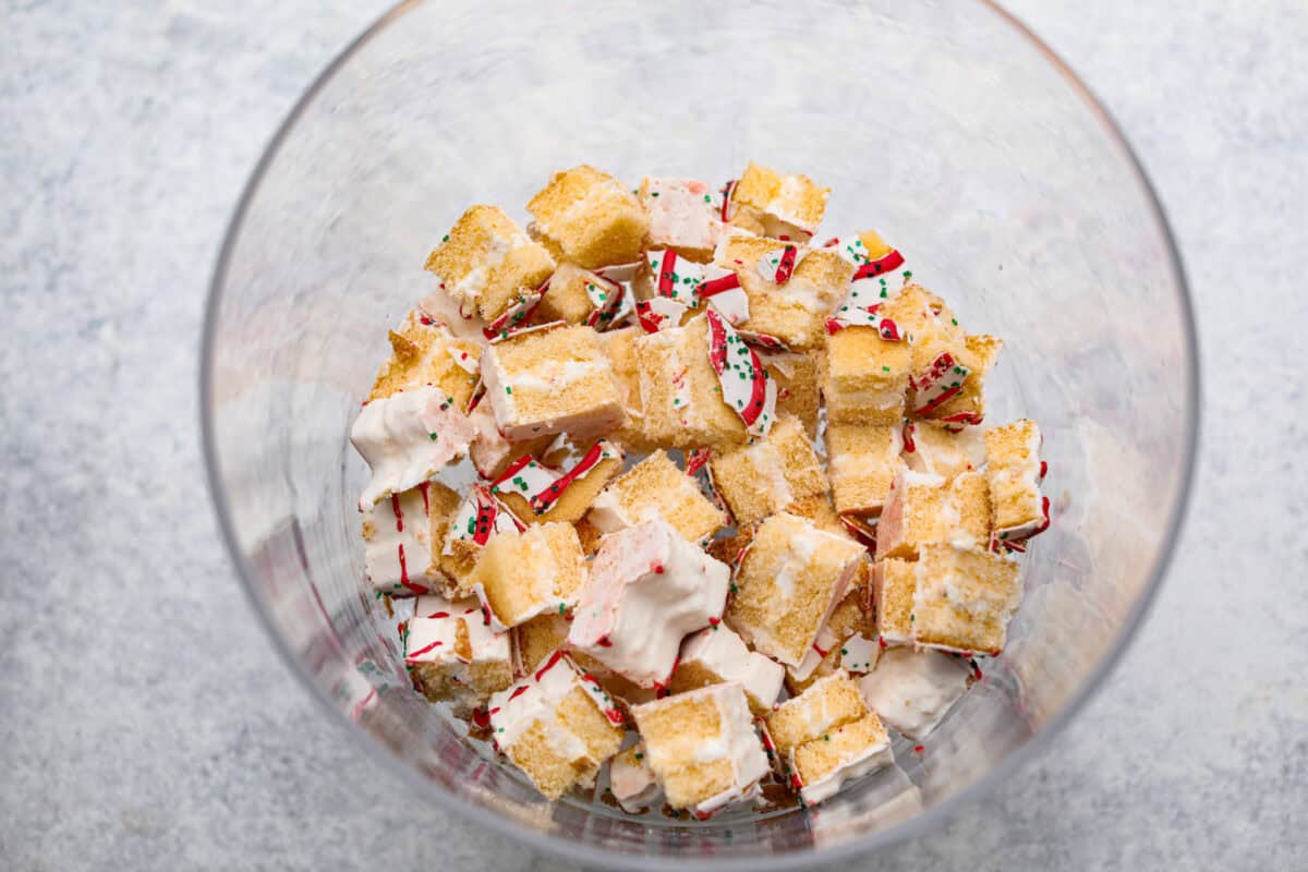 Little Debbie Christmas tree trifle is super adorable and tastes amazing! It's filled with sweet strawberries, creamy cream cheese, whipped topping flavored fluff, and chunks of the iconic Little Debbie Christmas trees. Overhead shot of Christmas tree cakes on the bottom of trifle dish.