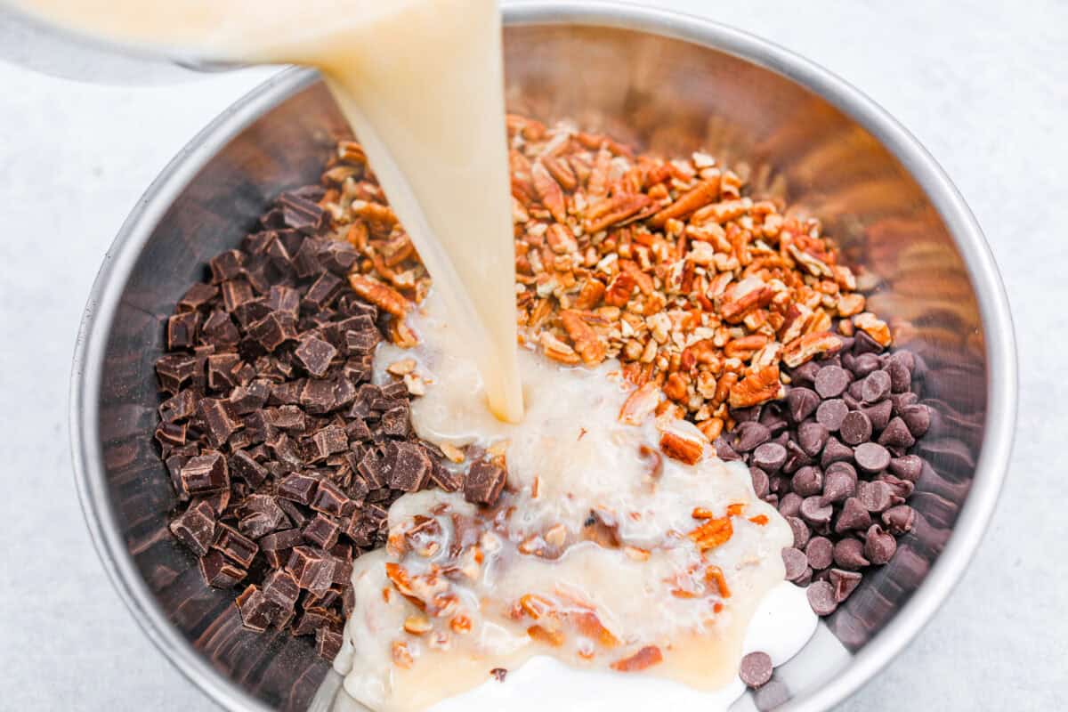 the sugar, butter, salt, and evaporated milk Overhead shot of the warm milk mixture being poured over the chocolate and nuts.