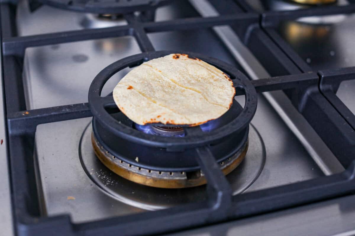Queso Fundido is a delicious cheesy appetizer with a kick from the Mexican chorizo. It's loaded with buttery, melty cheeses and covered in spicy chorizo sausage. Angle shot of a corn tortilla straight on a gas burner.