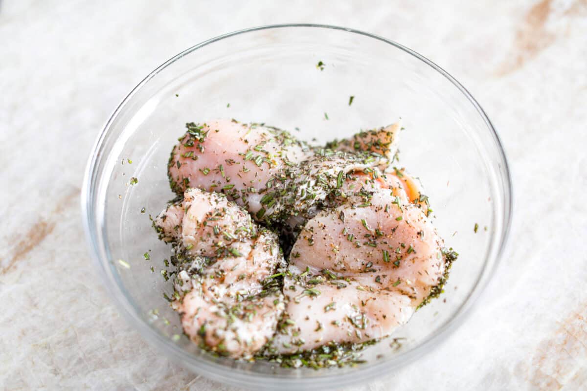 Rosemary Chicken is an incredibly simple yet flavorful dish you can whip up in no time. The infusion of butter with savory shallots, bright lemon juice, fresh rosemary, and tender seared chicken is an explosion of flavor. Overhead shot of chicken breasts with olive oil, lemon juice rosemary salt and pepper in a bowl.