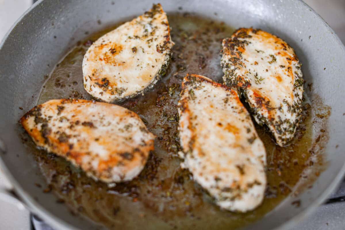 Rosemary Chicken is an incredibly simple yet flavorful dish you can whip up in no time. The infusion of butter with savory shallots, bright lemon juice, fresh rosemary, and tender seared chicken is an explosion of flavor. Close up shot of chicken breasts searing on a skillet.