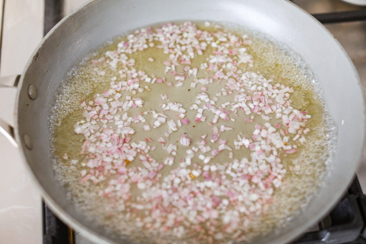Rosemary Chicken is an incredibly simple yet flavorful dish you can whip up in no time. The infusion of butter with savory shallots, bright lemon juice, fresh rosemary, and tender seared chicken is an explosion of flavor. Overhead shot of grape juice and shallots in a saucepan.