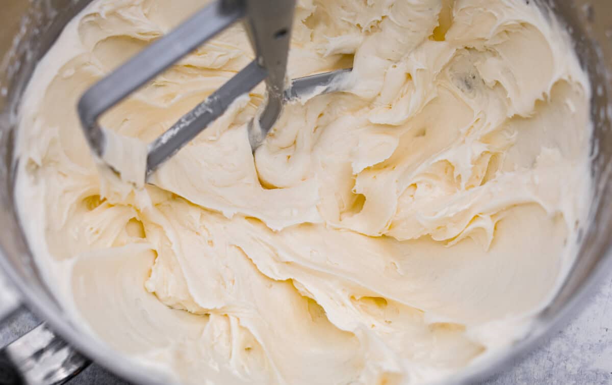 Tom Cruise coconut cake is a dense pound cake with coconut flavor and silky white chocolate throughout. The indulgent frosting is a coconut cream cheese buttercream with sweetened coconut on the outside. It's a coconut lover's dream—but a super sweet one. Overhead shot of the coconut frosting being whipped until fluffy in a mixing bowl.