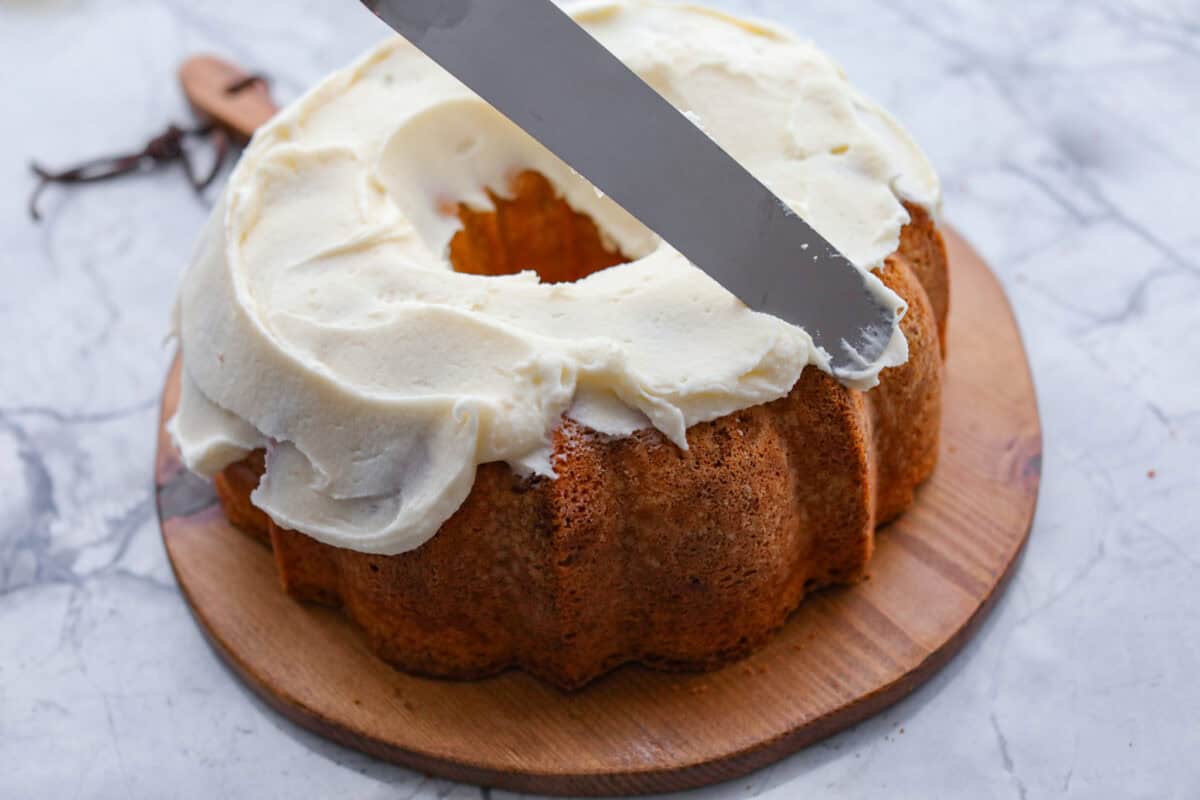 Tom Cruise coconut cake is a dense pound cake with coconut flavor and silky white chocolate throughout. The indulgent frosting is a coconut cream cheese buttercream with sweetened coconut on the outside. It's a coconut lover's dream—but a super sweet one. Angle shot of someone spreading the frosting on the cooked bundt cake.