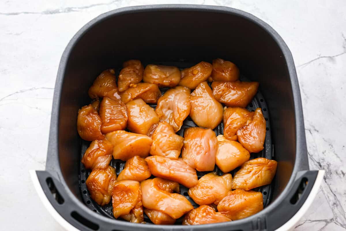 Super flavorful Air Fryer Teriyaki Chicken cooks up perfectly every time! It's tender and juicy on the inside, with a tasty teriyaki sauce coating the outside. Pair with rice and veggies for an easy meal on busy nights! Overhead shot of marinated chicken in the bottom of an air fryer basket.