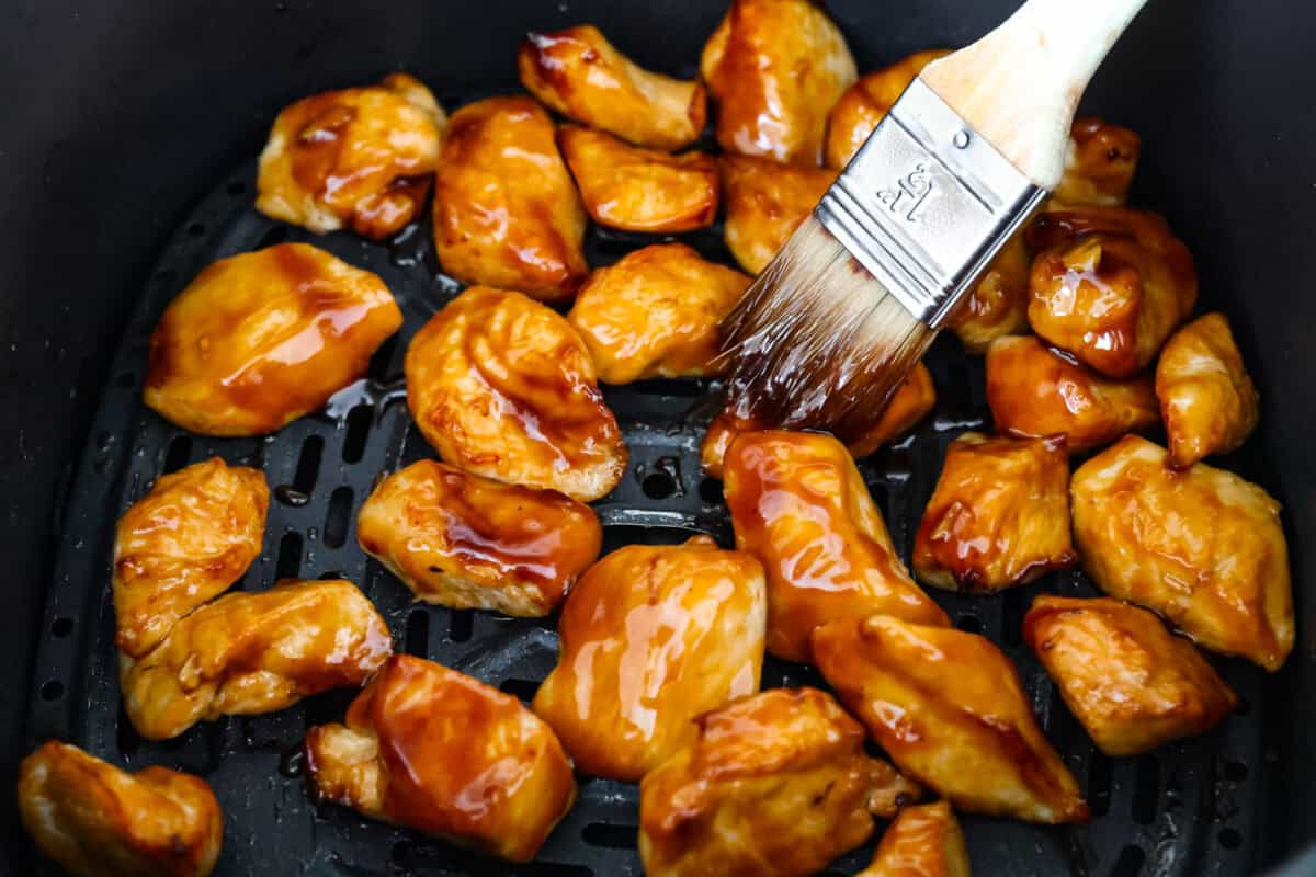 Super flavorful Air Fryer Teriyaki Chicken cooks up perfectly every time! It's tender and juicy on the inside, with a tasty teriyaki sauce coating the outside. Pair with rice and veggies for an easy meal on busy nights! Overhead shot of someone smearing chicken with teriyaki sauce.