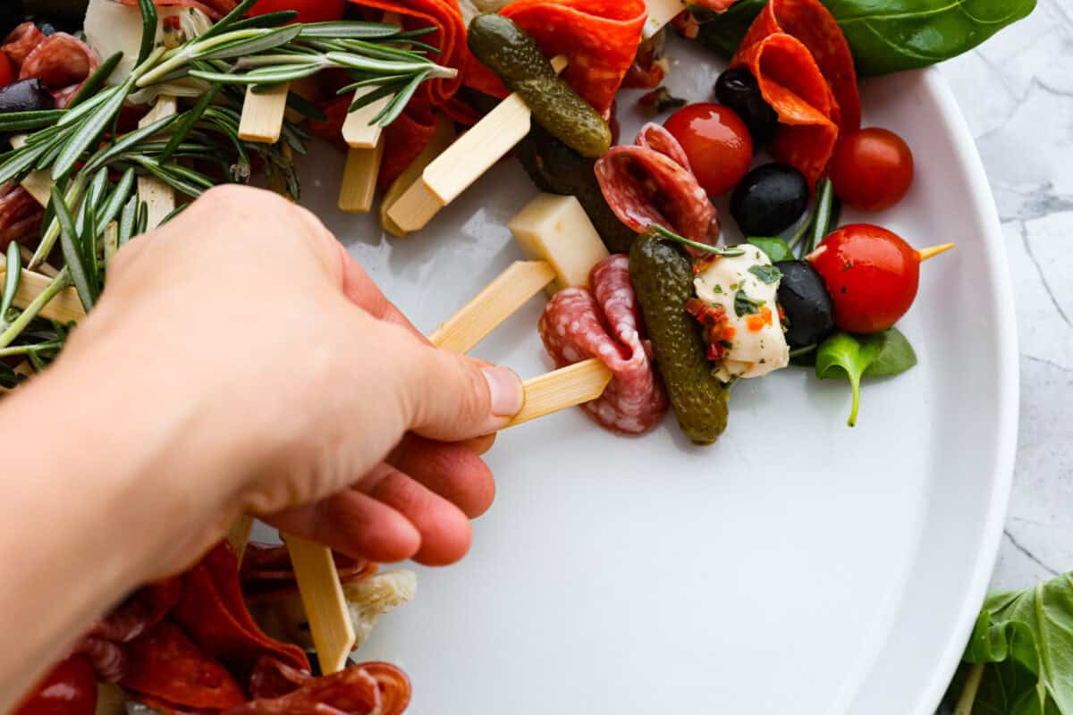 Bring this antipasto charcuterie wreath to your next holiday party! Skewered cheese, deli meats, olives, and pickles shaped into a cute Christmas wreath. A perfect festive appetizer to impress your guests! Third photo of arranging and shaping the antipasto charcuterie wreath.