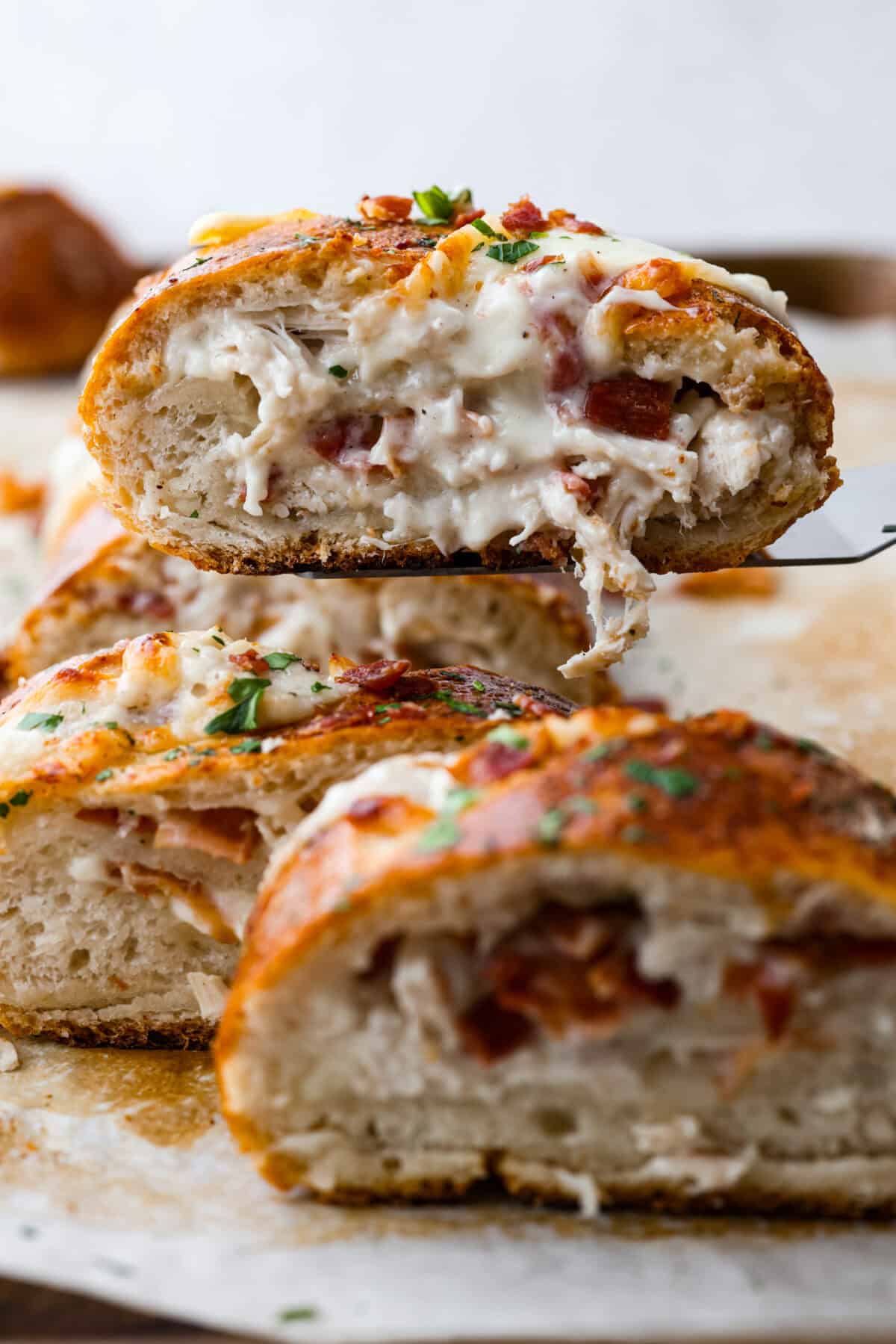 This Chicken Bacon Ranch Stromboli combines the tasty trio of tender chicken, crispy bacon, and creamy ranch dressing, all wrapped in golden pizza dough. It’s quick to prep and packed with flavor. Side shot of someone lifting a piece of the chicken bacon wrapped Stromboli with a spatula.