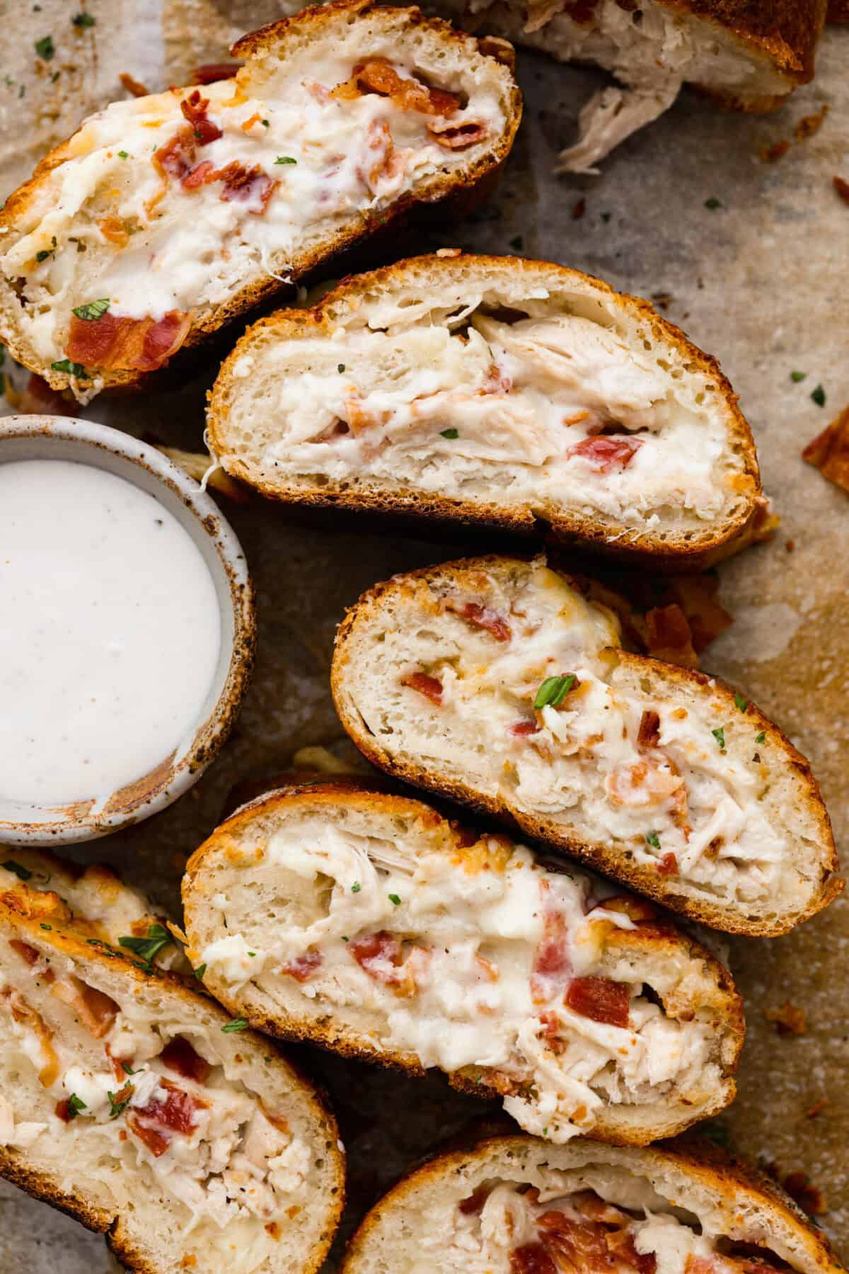 This Chicken Bacon Ranch Stromboli combines the tasty trio of tender chicken, crispy bacon, and creamy ranch dressing, all wrapped in golden pizza dough. It’s quick to prep and packed with flavor. Overhead shot of the chicken bacon ranch Stromboli cut and flipped on its side next to a side of ranch.