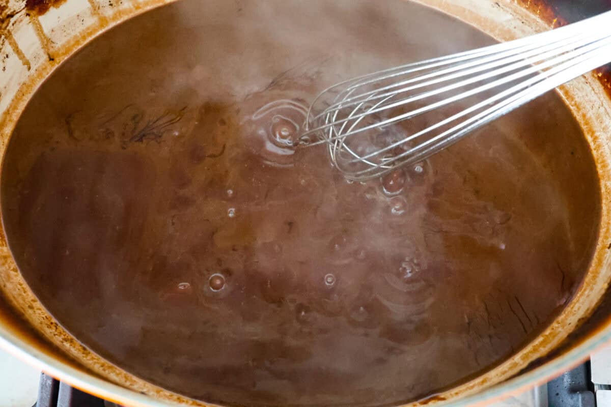Tender braised short ribs will fall off the bone and leave you speechless! Seared then cooked in a red wine reduction, beef broth, and fresh herbs. Every bite is tender perfection and will melt in your mouth! Eighth photo of the gravy cooking and over the stove.